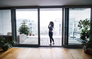 Woman talking on her phone while standing on a large balcony | Featured image for The What Are the Best Blinds for Sliding Doors Blog by Cosmopolitan Shutters.