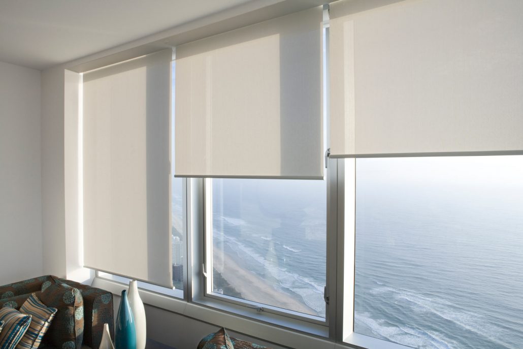 Window blinds opening up to reveal ocean views | Featured image for the Sunshine Coast Location Page from Cosmopolitan Shutters.