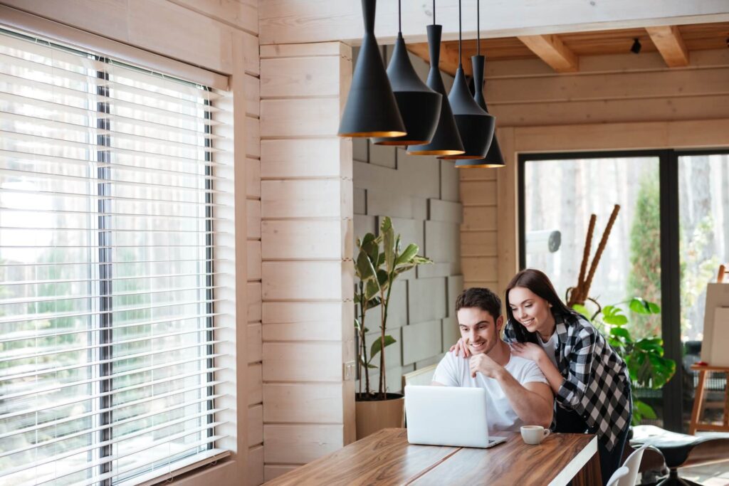 Woman and man looking at a laptop that is on a large table | Featured image for The What Are the Best Window Coverings to Keep Heat Out Blog by Cosmopolitan Shutters.